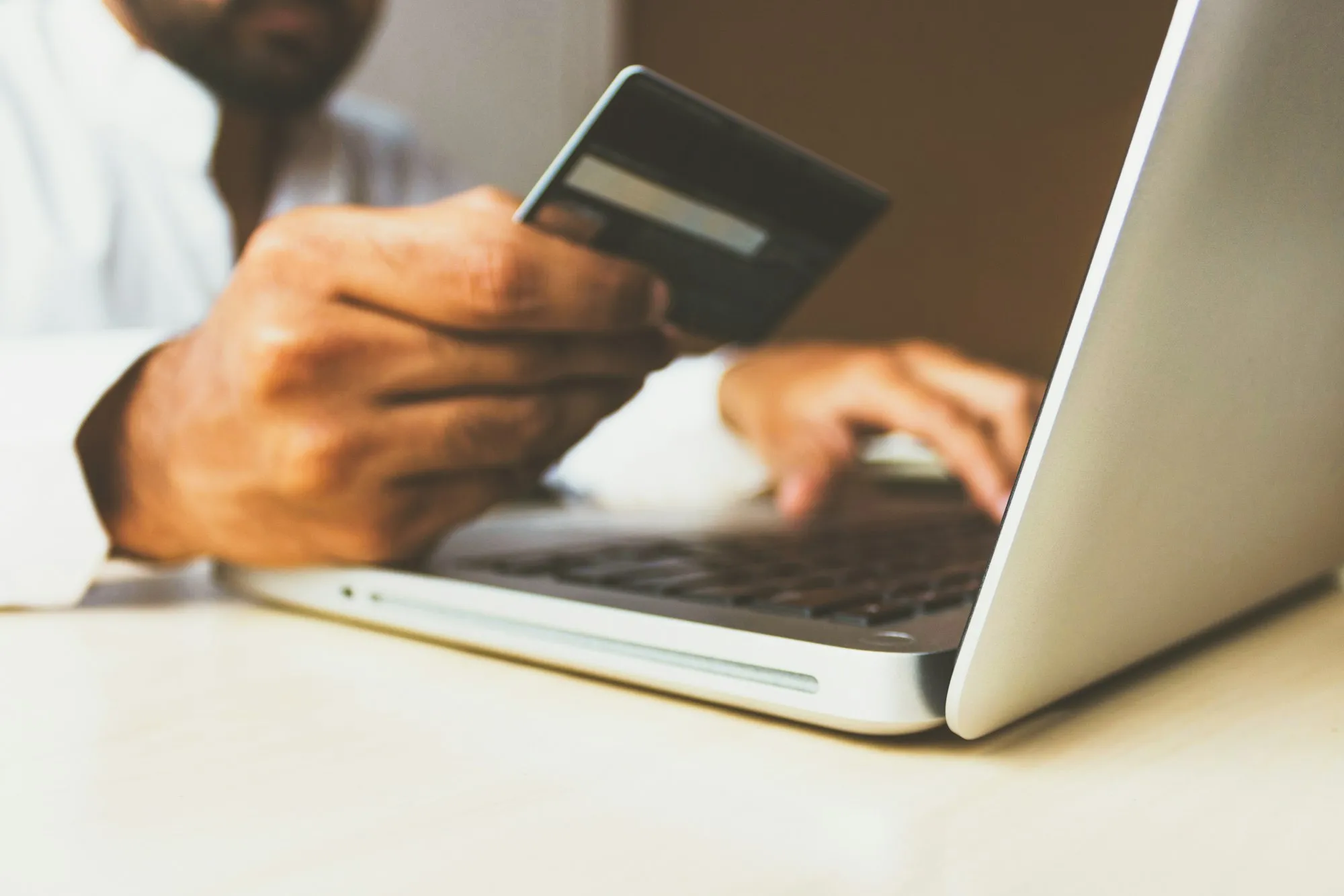 A person holding a credit card while typing on an open laptop