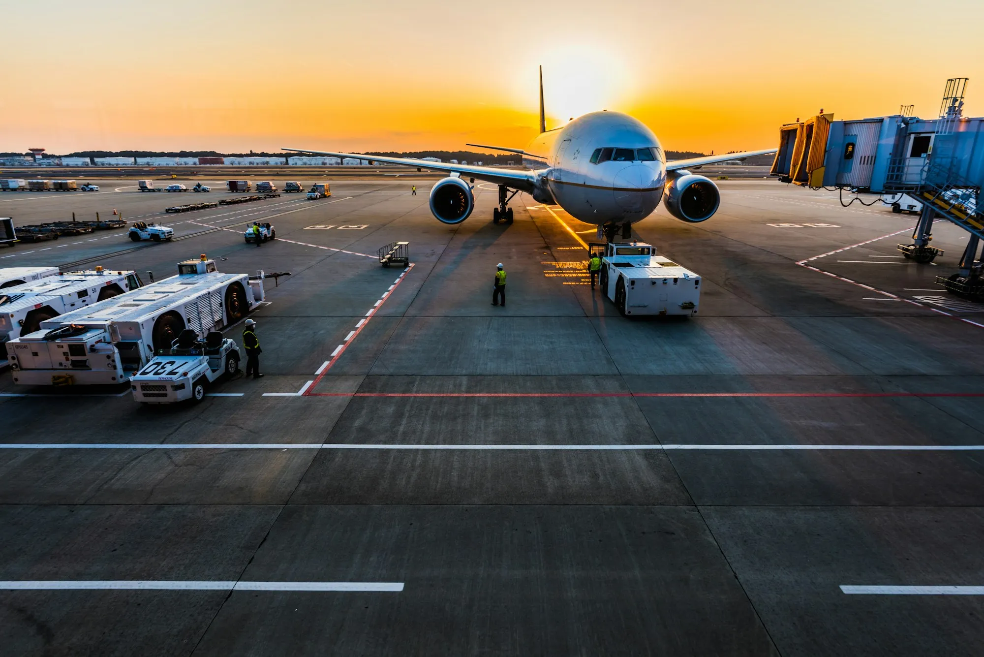 A widebody jet surrounded by ground vehicles at the gate at sunrise