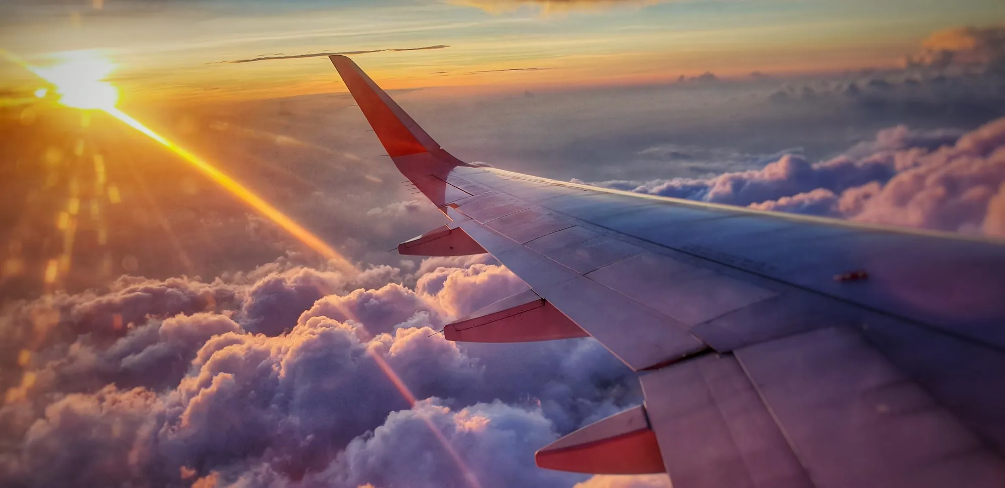 An aircraft wing over sunset clouds, seen through a passenger window