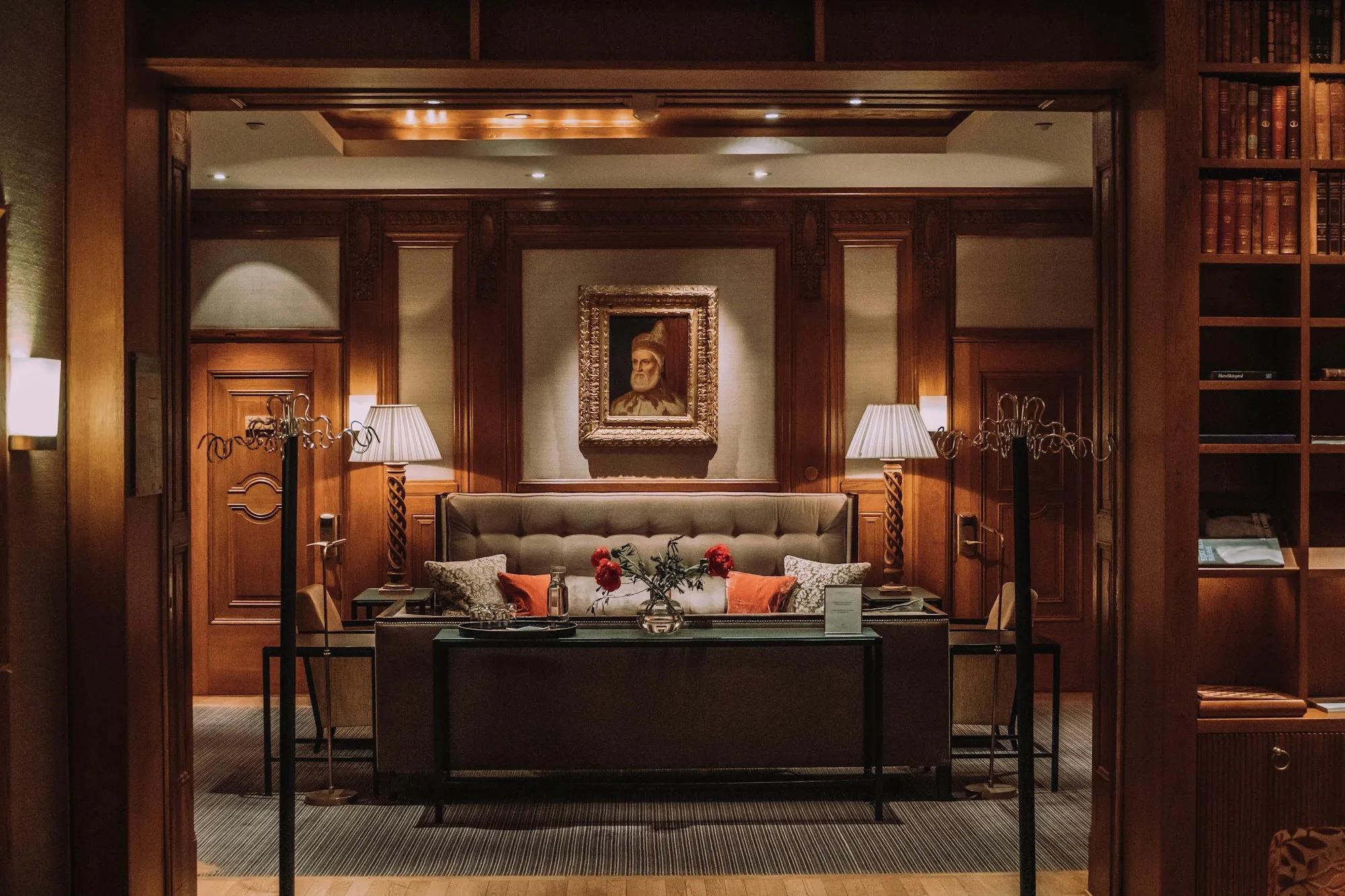 A warmly lit wood-paneled lounge with lamps, a tufted sofa and bookshelves