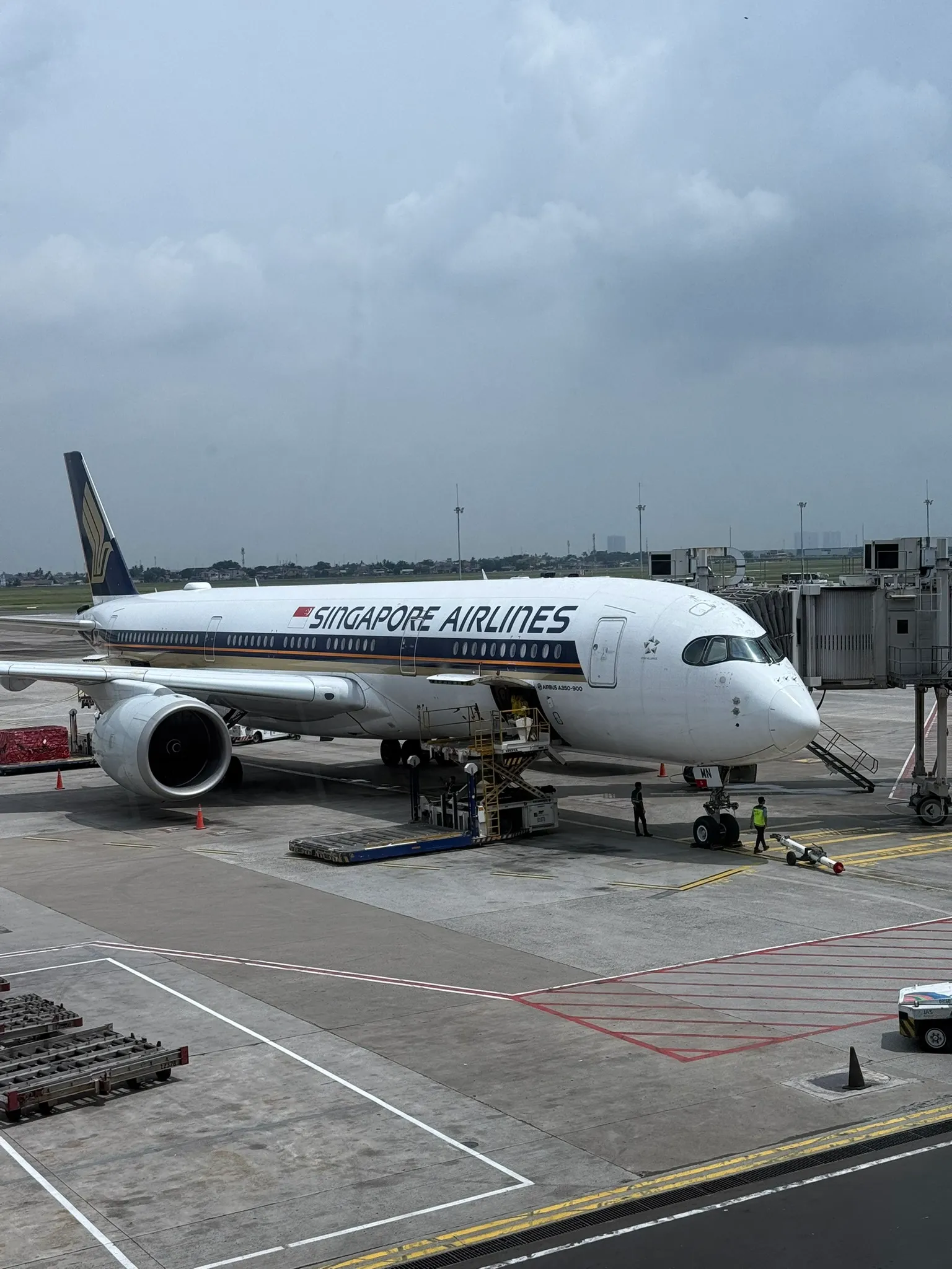 A Singapore Airlines Airbus A350-900 parked at a jet bridge, being loaded