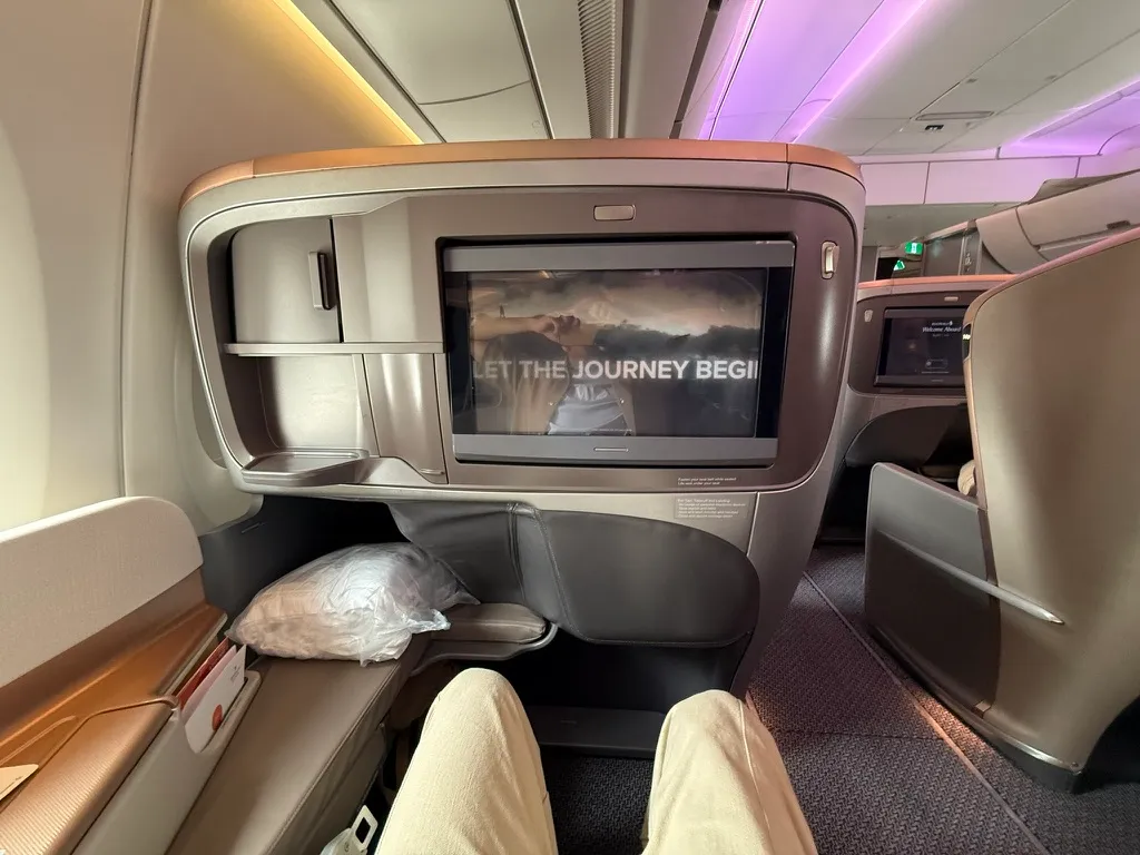A Singapore Airlines business class seat with the entertainment screen displaying a welcome message
